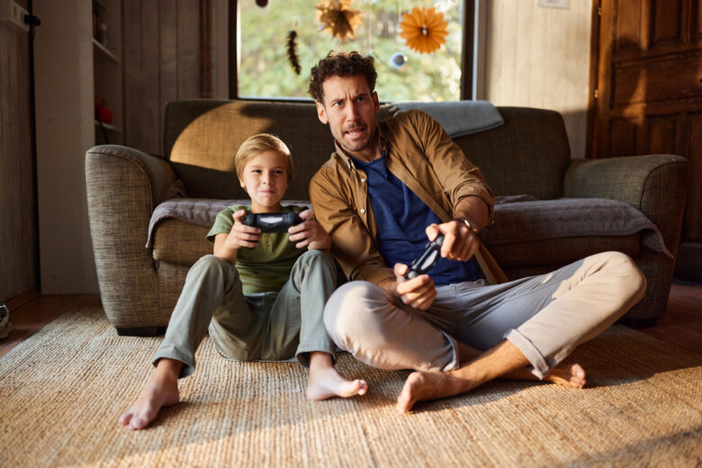 Carefree single father and his son having fun while playing video games on TV in the living room.