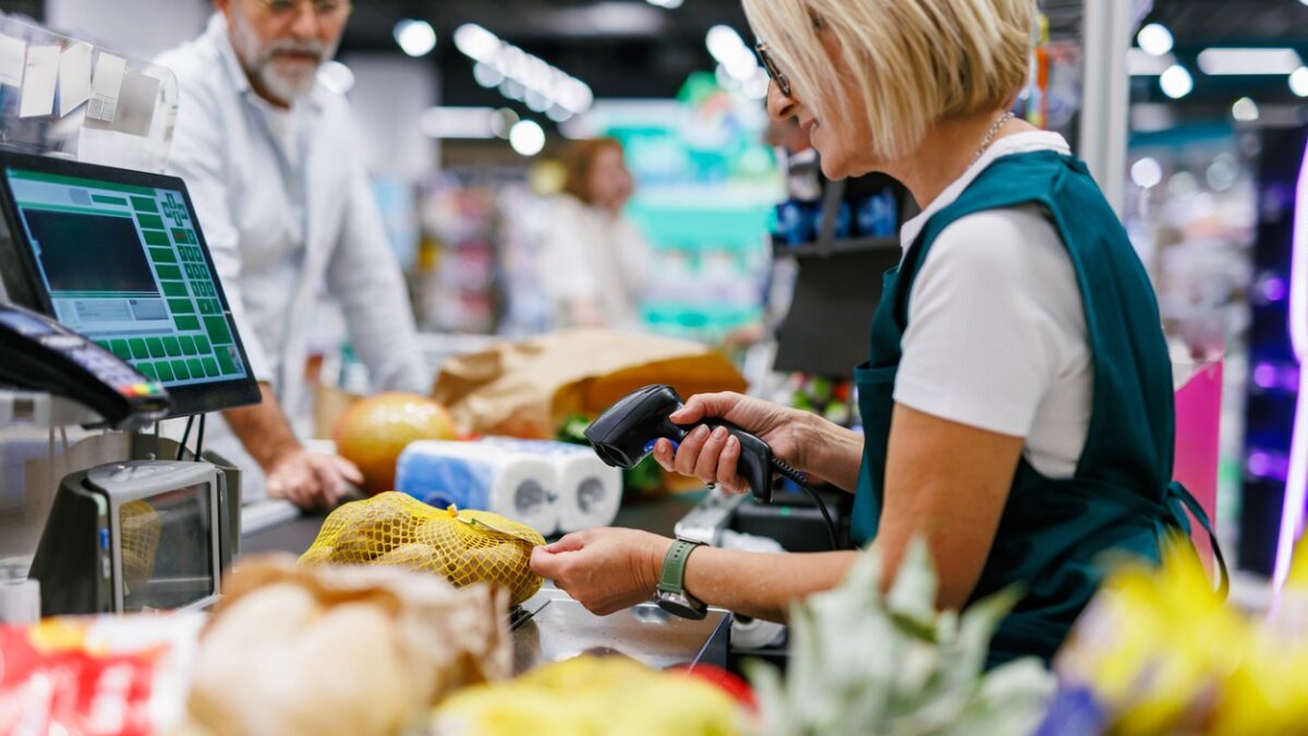 Supermarket cashier scanning groceries at the checkout with barcode reader while customer is waiting, cashier and clients are not recognizable