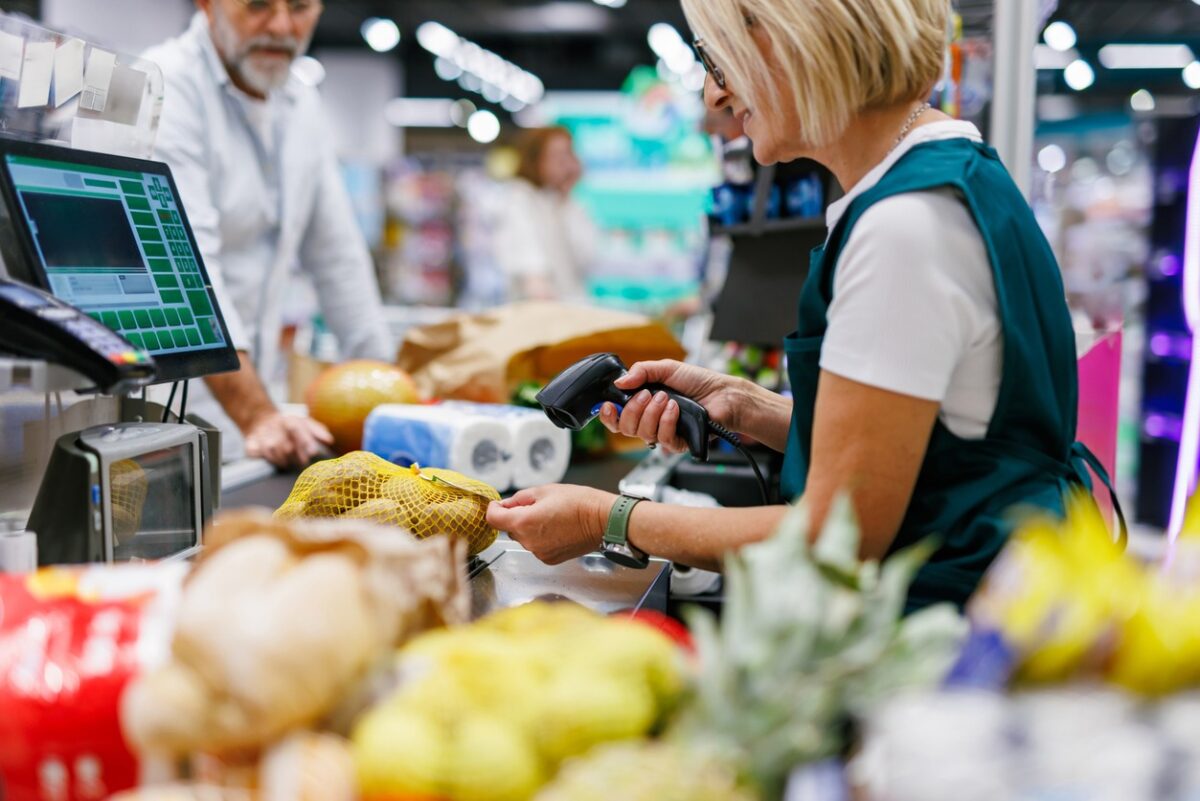 Supermarket cashier scanning groceries at the checkout with barcode reader while customer is waiting, cashier and clients are not recognizable