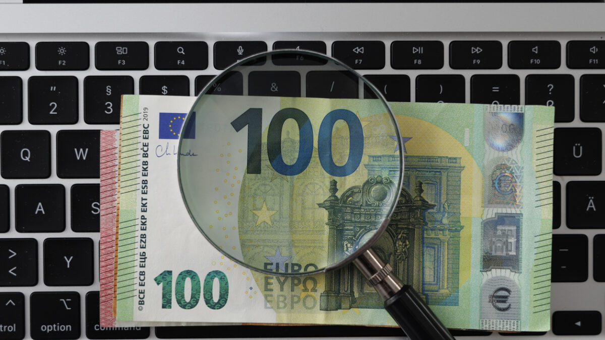 Magnifying glass on Euro banknote and laptop – concept of searching for online income