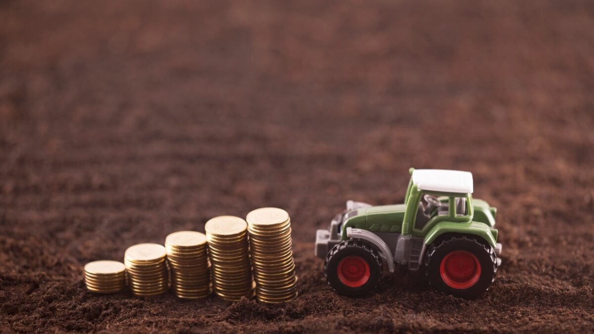 Tractor miniature with coins on fertile soil land