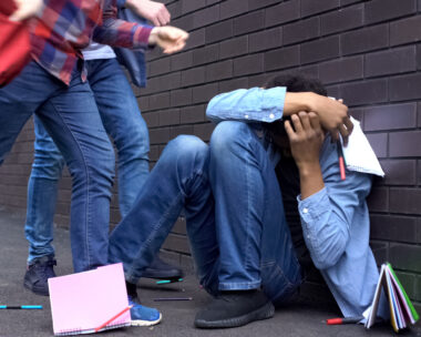 Cruel teenagers scattering classbooks of afro-american boy, school bullying