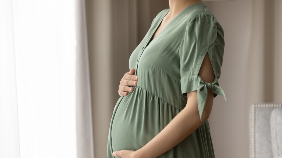 Expectant mother wearing dress for pregnant, holding big baby bump, feeling kicks, touching and hugging belly with love and care. Childbirth, pregnancy, clothes for expecting concept