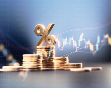 Percentage sign on top of coin stacks before blue financial graph. Horizontal composition with copy space. Business and finance concept.