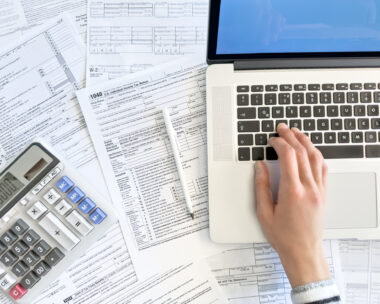Close up photo of a woman doing taxes with laptop and tax forms in a house