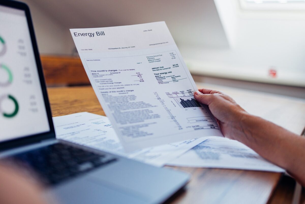 A person reviews their energy bill while using a laptop at home. The document includes various charges and electricity usage information