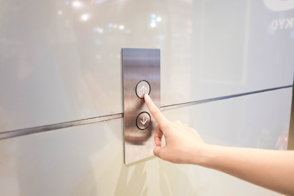 Cropped Hand Of Woman Pressing Push Button For Elevator On Wall