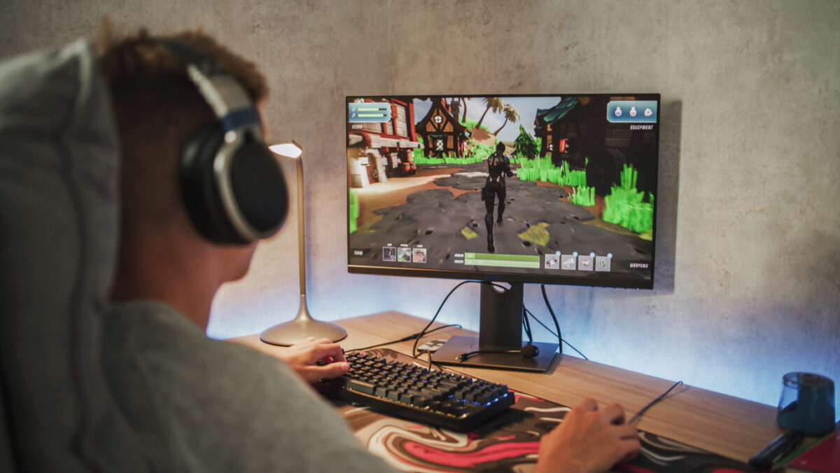 Caucasian teenager wearing headphones plays online video game on PC, spends leisure time at home. Professional young gamer enjoys gameplay in 3D third person shooter on computer. Gaming and Esports