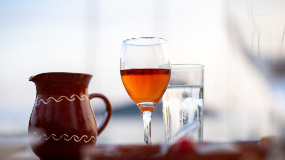 A glass of rose wine on a table with a clay jug and water glass