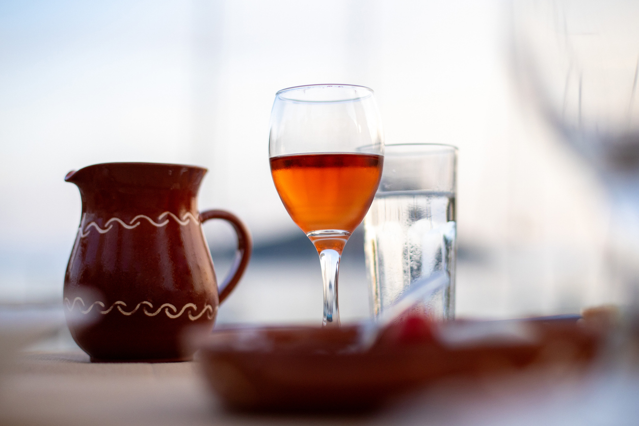 A glass of rose wine on a table with a clay jug and water glass