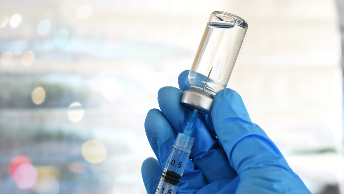 Medical personnel filling a syringe needle with generic vaccine booster from vial