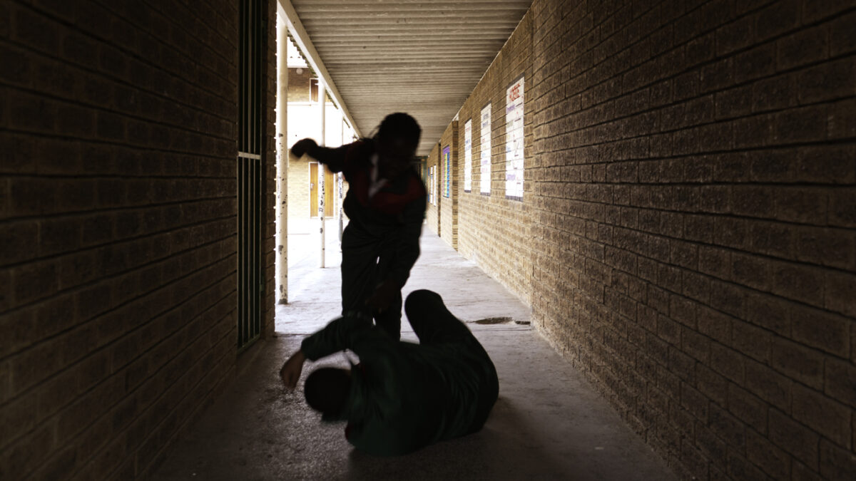 Two school kids fight in a dark passageway of their school, almost silhouette