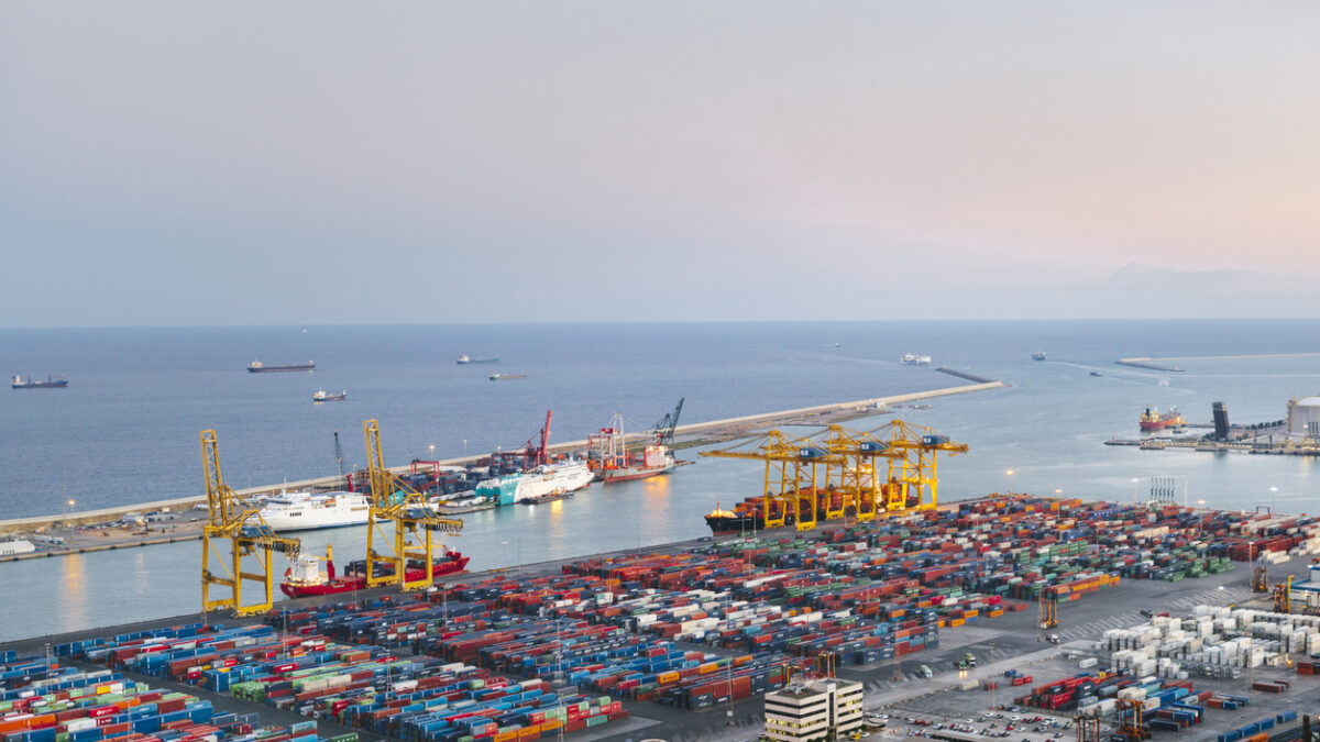 Barcelona commercial dock at dusk with containers and cranes.