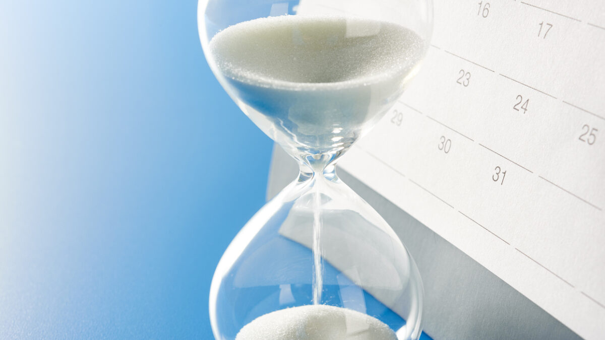 Hourglass and calendar. On office desk table. With copy space.