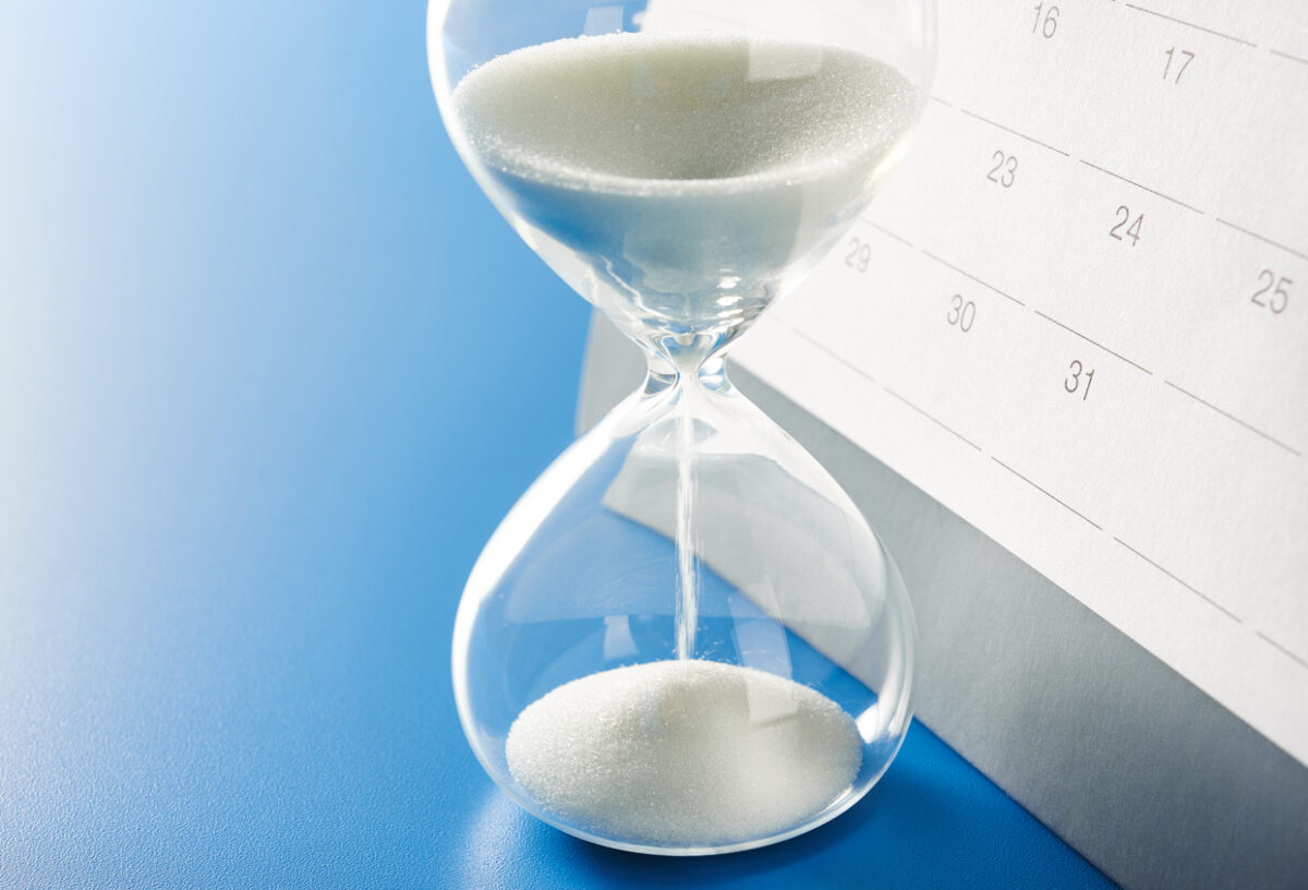 Hourglass and calendar. On office desk table. With copy space.