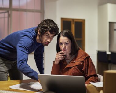 Businessman discussing over laptop with businesswoman at home office. Male and female entrepreneurs are planning strategy over laptop. They are working late in apartment.
