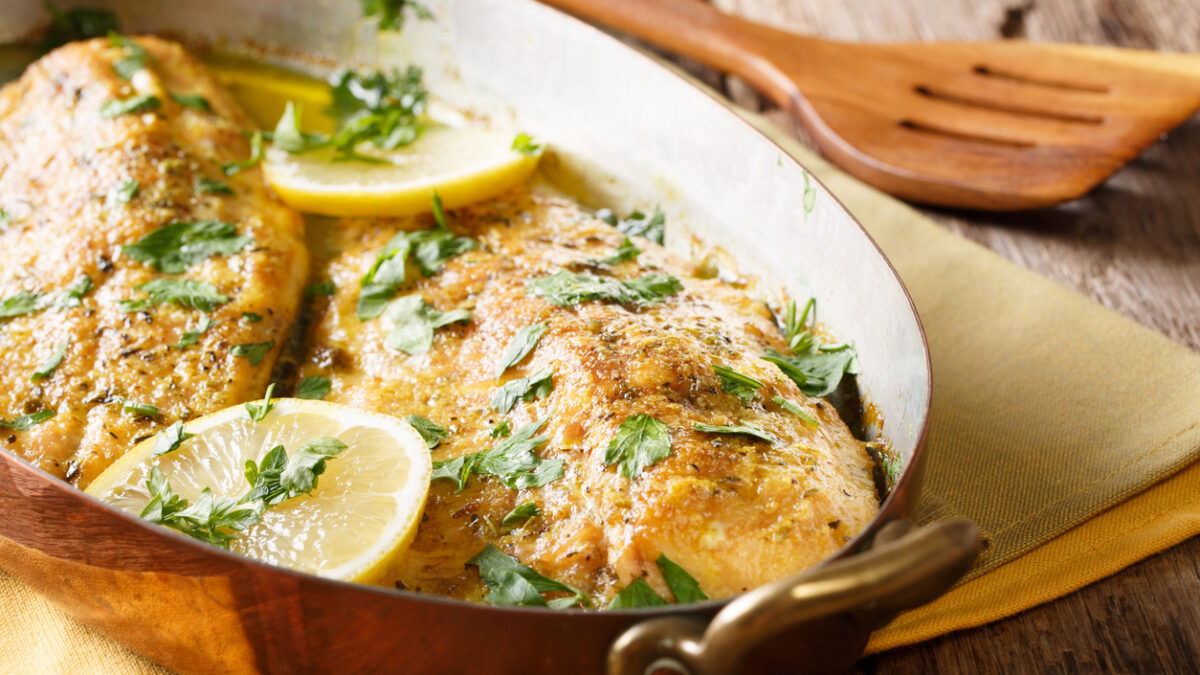 Delicious fish: baked trout fillets with garlic buttery herb sauce, lemon and parsley close-up in a copper frying pan. horizontal