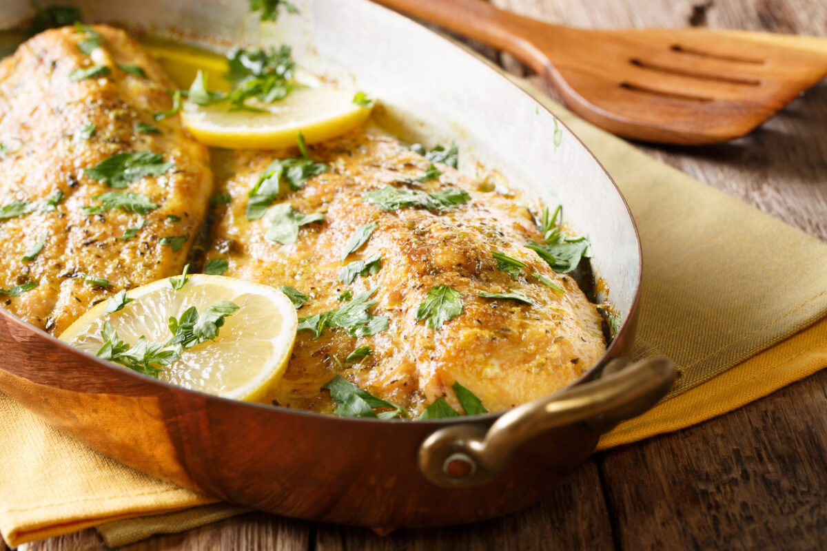 Delicious fish: baked trout fillets with garlic buttery herb sauce, lemon and parsley close-up in a copper frying pan. horizontal