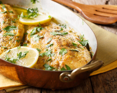 Delicious fish: baked trout fillets with garlic buttery herb sauce, lemon and parsley close-up in a copper frying pan. horizontal