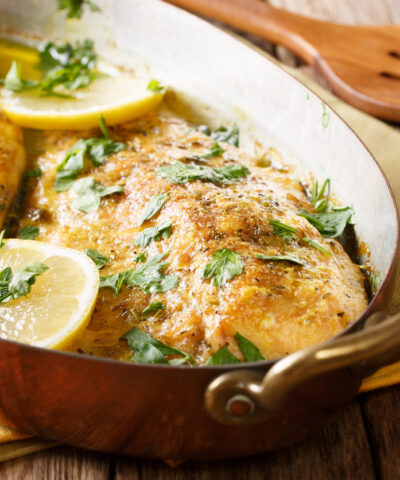 Delicious fish: baked trout fillets with garlic buttery herb sauce, lemon and parsley close-up in a copper frying pan. horizontal