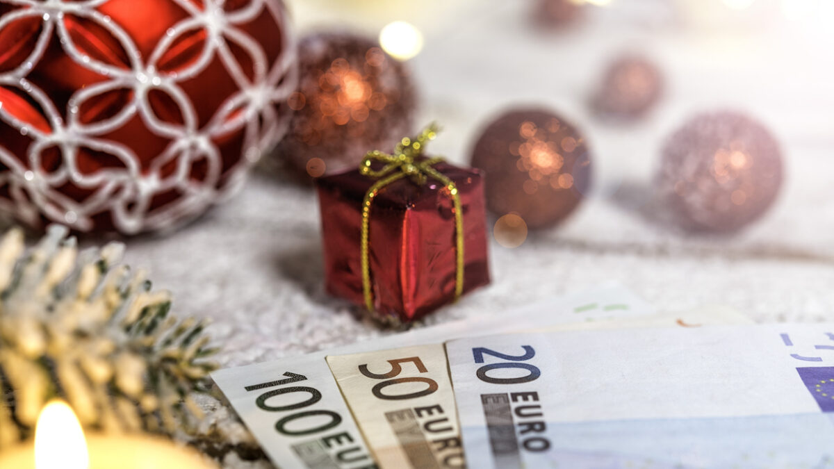 Christmas ball on old wooden table with candle and Euro banknotes