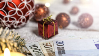 Christmas ball on old wooden table with candle and Euro banknotes