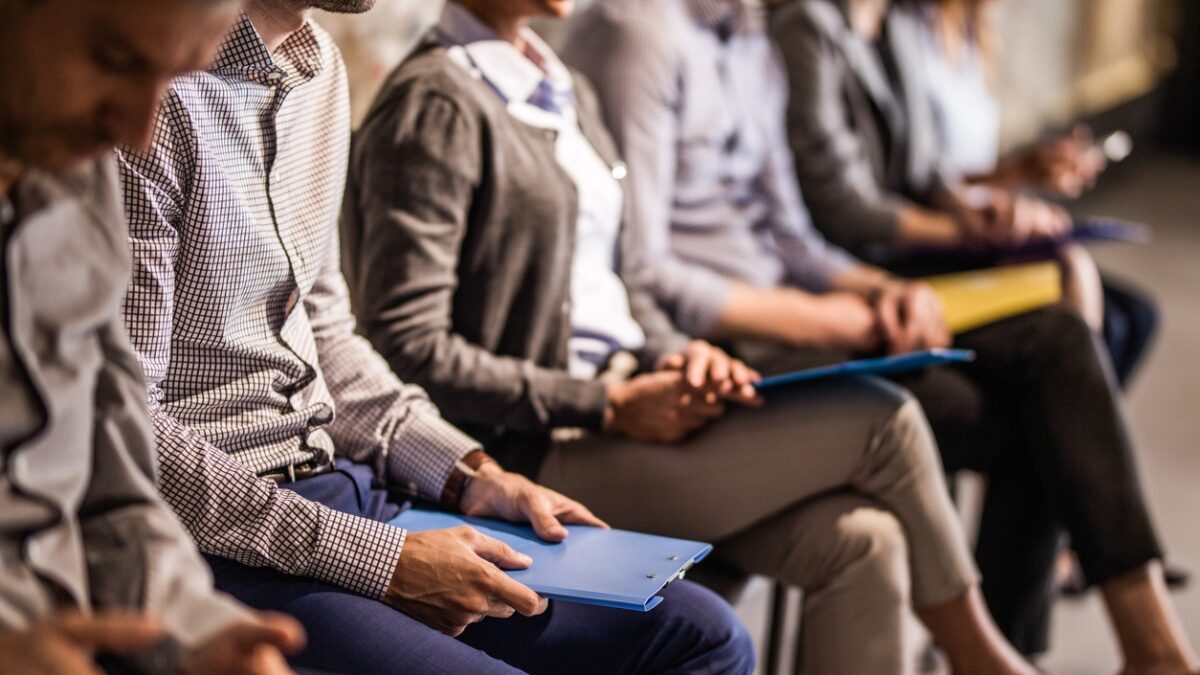 Large group of unrecognizable business people waiting for a job interview. Focus is on man with blue clipboard.