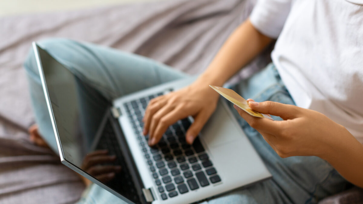Woman with credit card in hands in front of laptop monitor - view from the top. Online shopping at home concept.