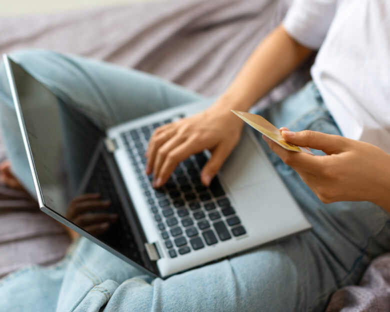 Woman with credit card in hands in front of laptop monitor - view from the top. Online shopping at home concept.