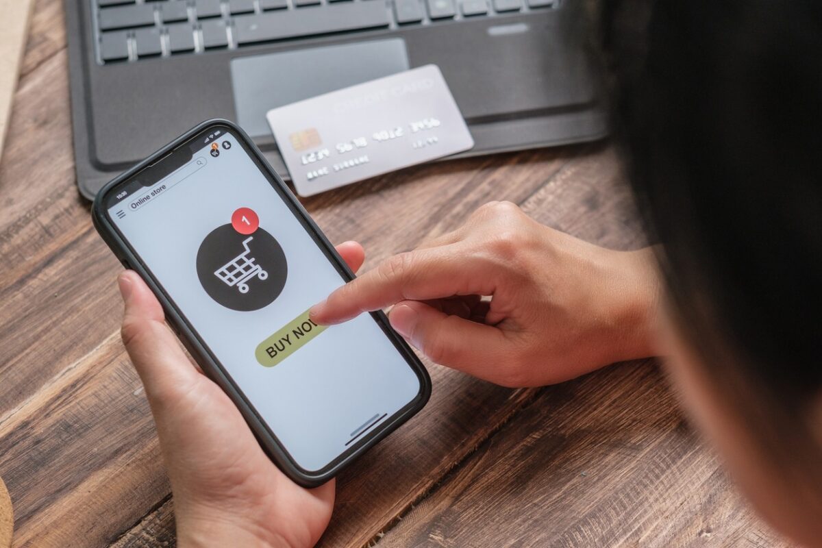 close up woman hand add product to card at shopping online mobile app on wood table at home
