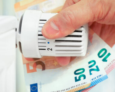 Hand on the heating thermostat with money bills, heating costs concept