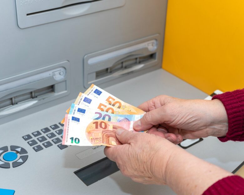 RETIRED SENIOR WOMAN WITHDRAWING MONEY FROM AN ATM. DIGITAL DIVIDE AMONG THE ELDERLY