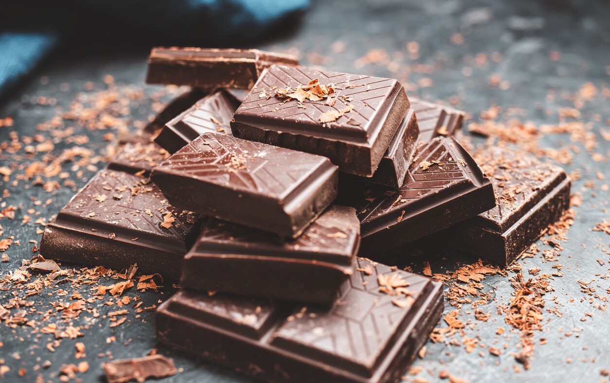 Dark chocolate bar pieces on dark background with grated chocolate, pile chunks of broken chocolate.