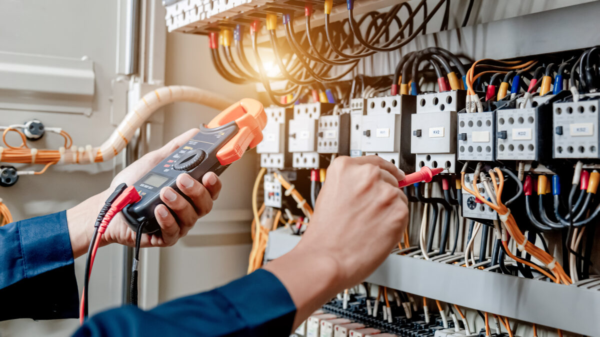 Electrician engineer uses a multimeter to test the electrical installation and power line current in an electrical system control cabinet.
