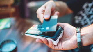 Adult man paying with credit card at cafe, close-up of hands with credit card and credit card reader