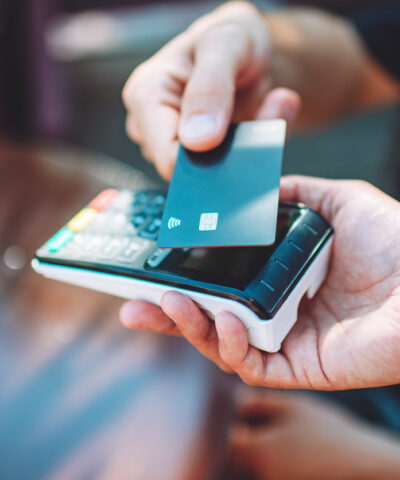 Adult man paying with credit card at cafe, close-up of hands with credit card and credit card reader