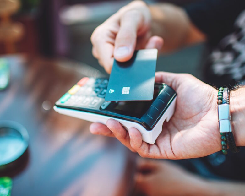 Adult man paying with credit card at cafe, close-up of hands with credit card and credit card reader