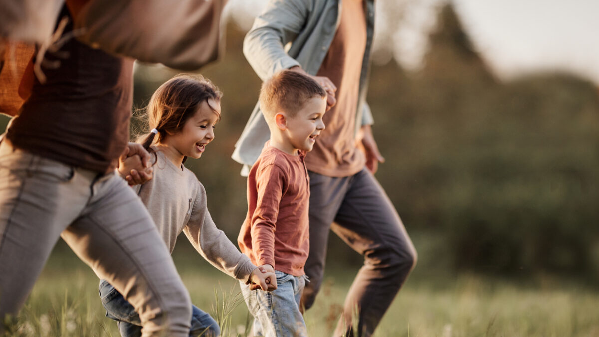 Happy siblings having fun while holding hands with their parents and running during spring day in nature. Copy space.