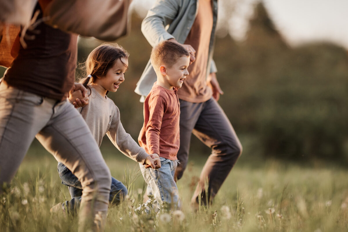 Happy siblings having fun while holding hands with their parents and running during spring day in nature. Copy space.
