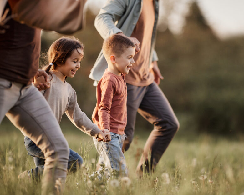 Happy siblings having fun while holding hands with their parents and running during spring day in nature. Copy space.