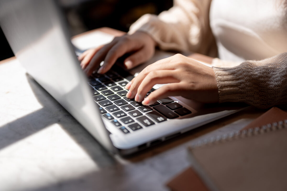 Close-up image of a woman typing on laptop keyboard, working on her laptop computer at a table indoors on a sunny day. businesswoman, student, digital nomad, working remotely