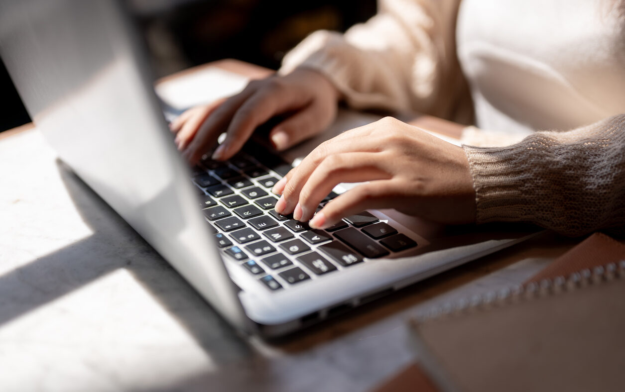 Close-up image of a woman typing on laptop keyboard, working on her laptop computer at a table indoors on a sunny day. businesswoman, student, digital nomad, working remotely