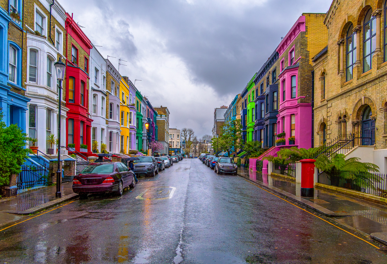 View of the wonderful Lancaster Road, the mythical street of colorful houses under a fine rain with a cloudy sky and pedestrians walking with umbrellas in Notting Hill, London, England.