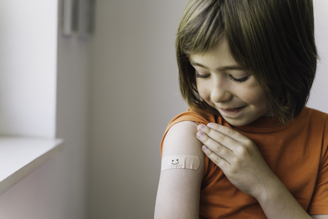 A young boy observes her vaccination band-aid with joy, illustrating a moment of personal triumph and the emotional connections children form with their health journeys.