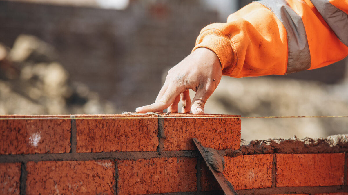 Bricklayer laying another brick in the wall on construction site for sturdy wall