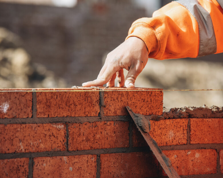 Bricklayer laying another brick in the wall on construction site for sturdy wall