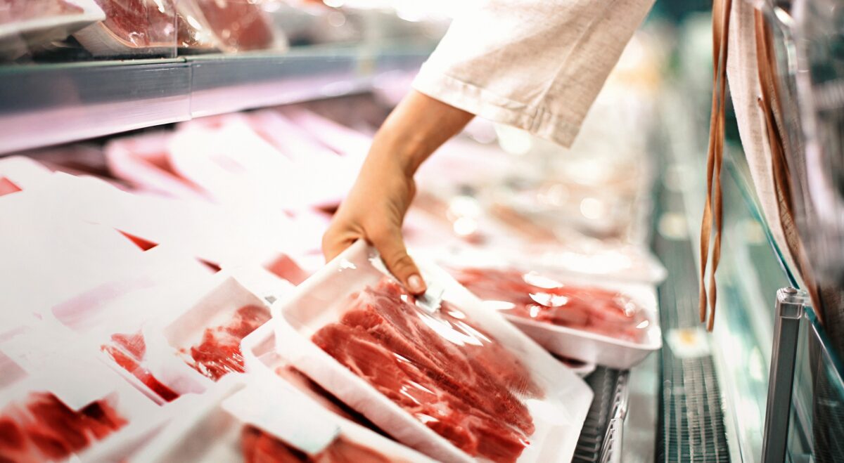 Closeup side view of unrecognizable woman chossing some fresh meat at local supermarket. The meat is cut into chops and packed into one pound packages. She has reached for a package of beef sirloin steaks