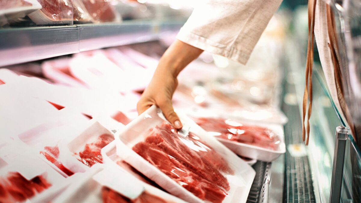Closeup side view of unrecognizable woman chossing some fresh meat at local supermarket. The meat is cut into chops and packed into one pound packages. She has reached for a package of beef sirloin steaks