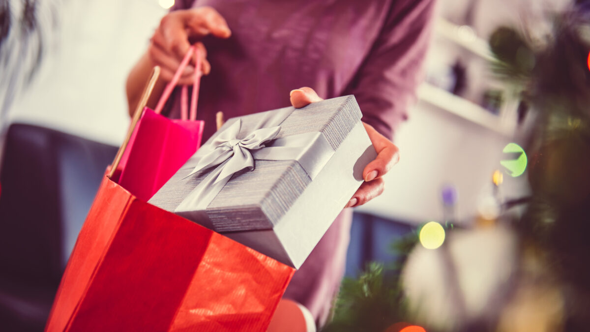 Woman standing by the christmas tree and taking a christmas present out of shopping bag