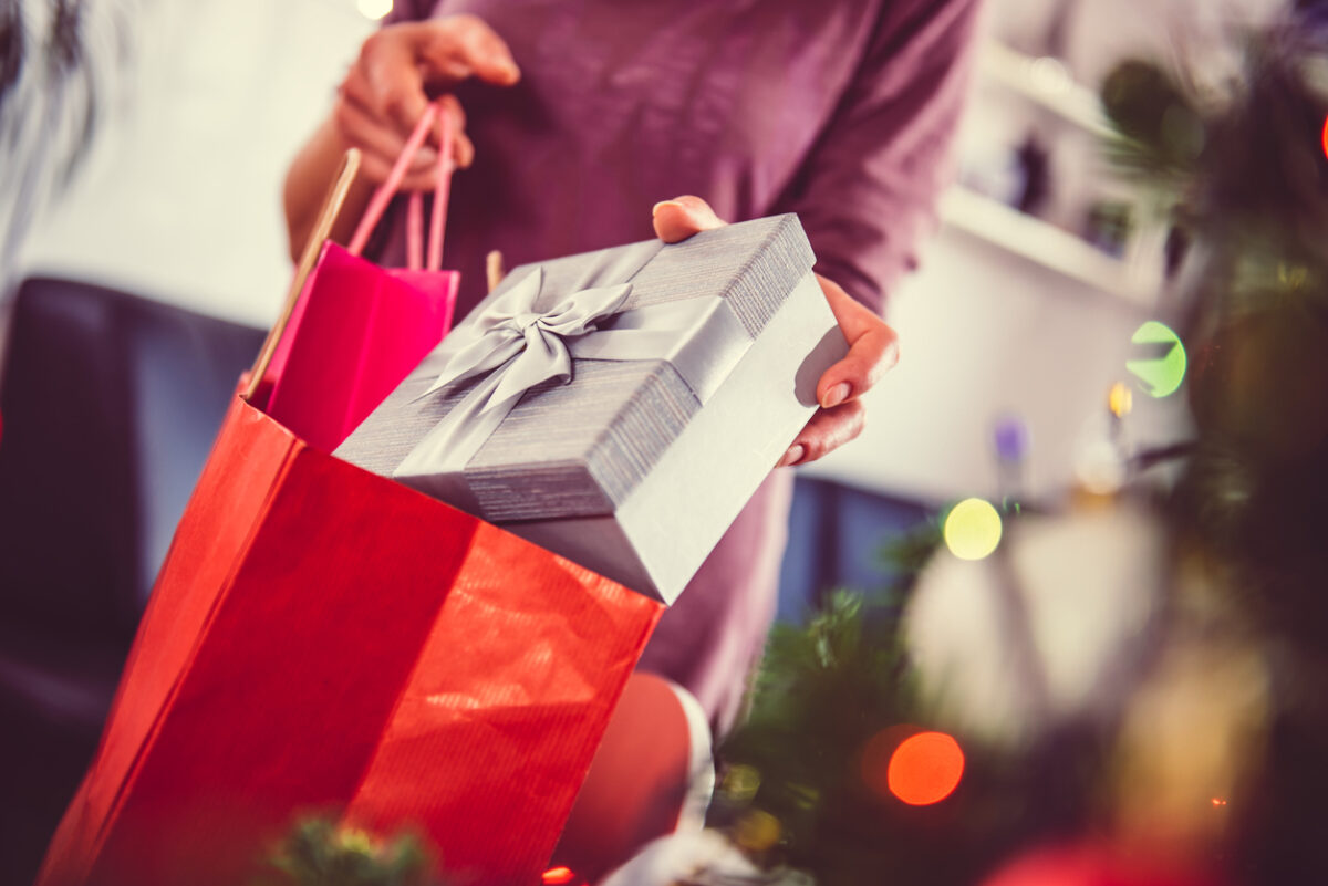 Woman standing by the christmas tree and taking a christmas present out of shopping bag